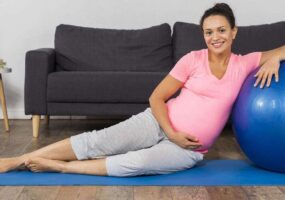 mujer embarazada sonriente en casa con colchoneta de ejercicios con pelota